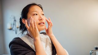 woman massaging her face in front of the mirror