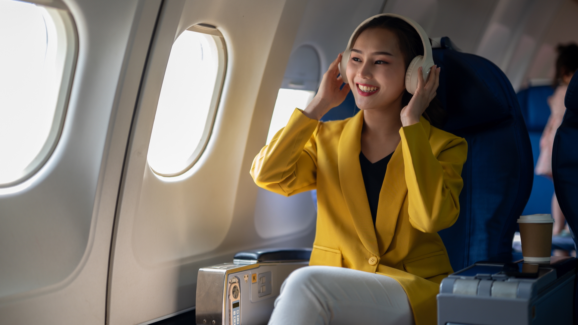 A woman on a plane smiling and wearing headphones
