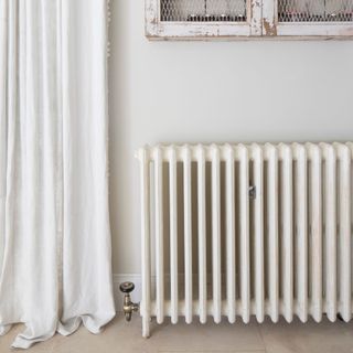 White painted walls with a white radiator on it, and white curtains hanging nearby