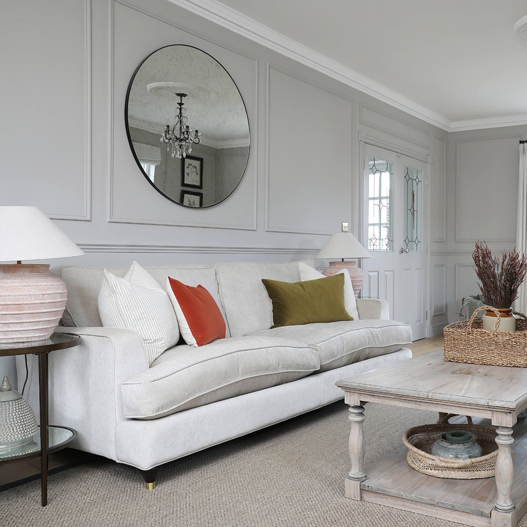 A light grey-painted living room with a cream sofa and a round mirror hung above it