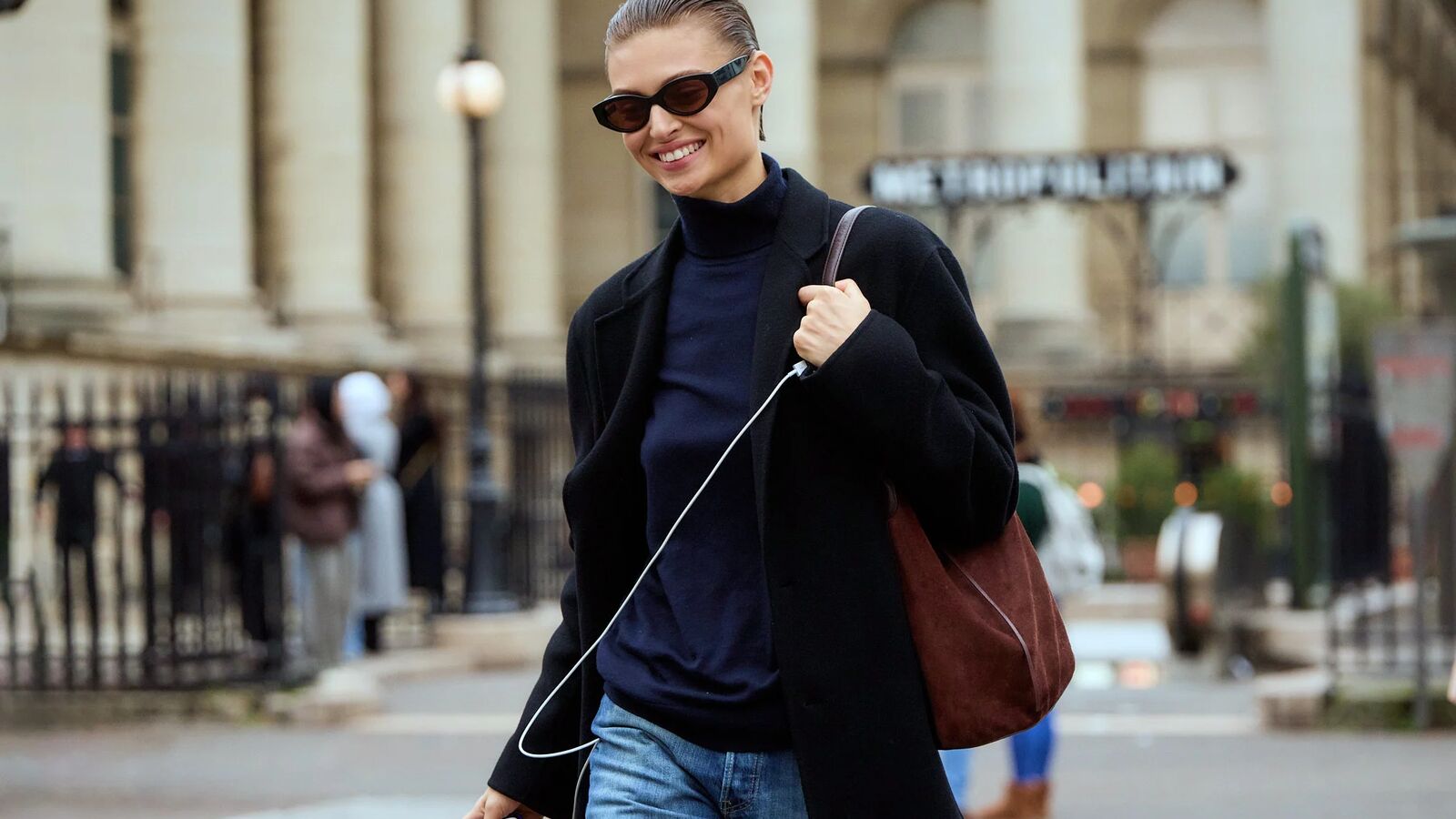 Woman wearing blue turtleneck, black coat, brown suede bag, and jeans in Paris.