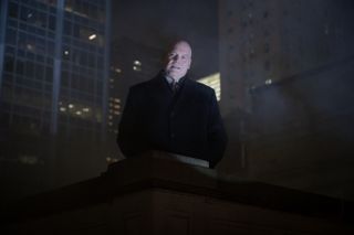 Wilson Fisk (Vincent D'Onofrio) stands on the top of a building in New York City, viewed from slightly below. It is very dark behind him and we can't see much else, but there are lights on in some of the skyscrapers in the distance.