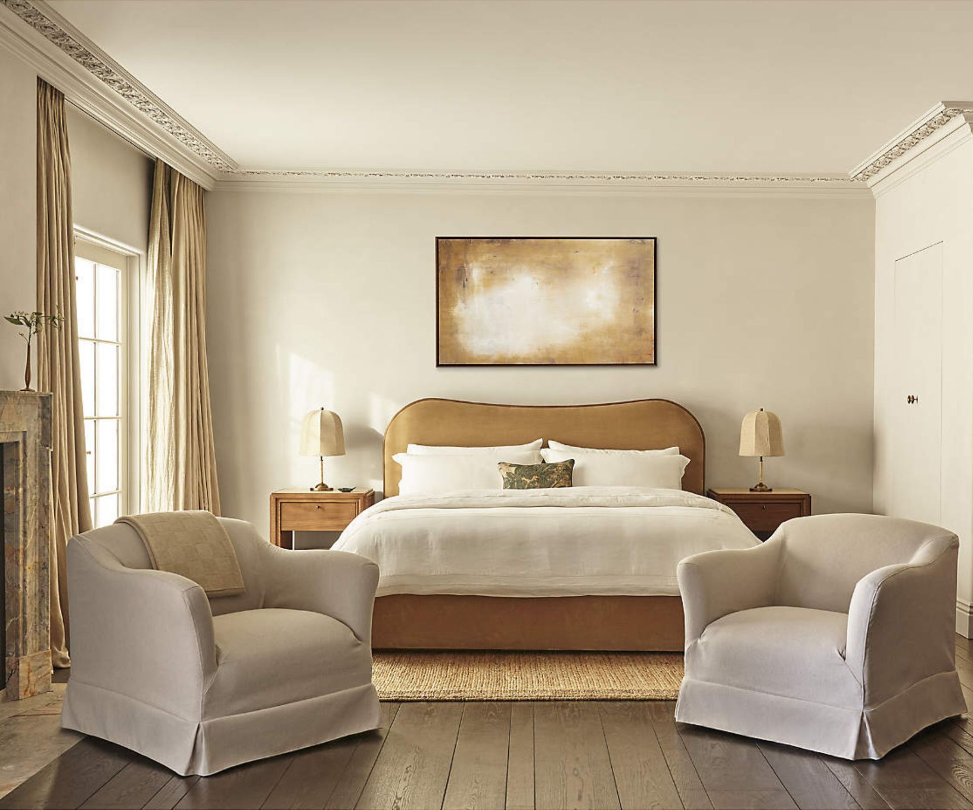 neutral bedroom with yellow velvet upholstered curved bed, white linens, and two neutral skirted arm chairs