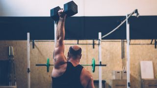Man in a gym holds dumbbell above his head