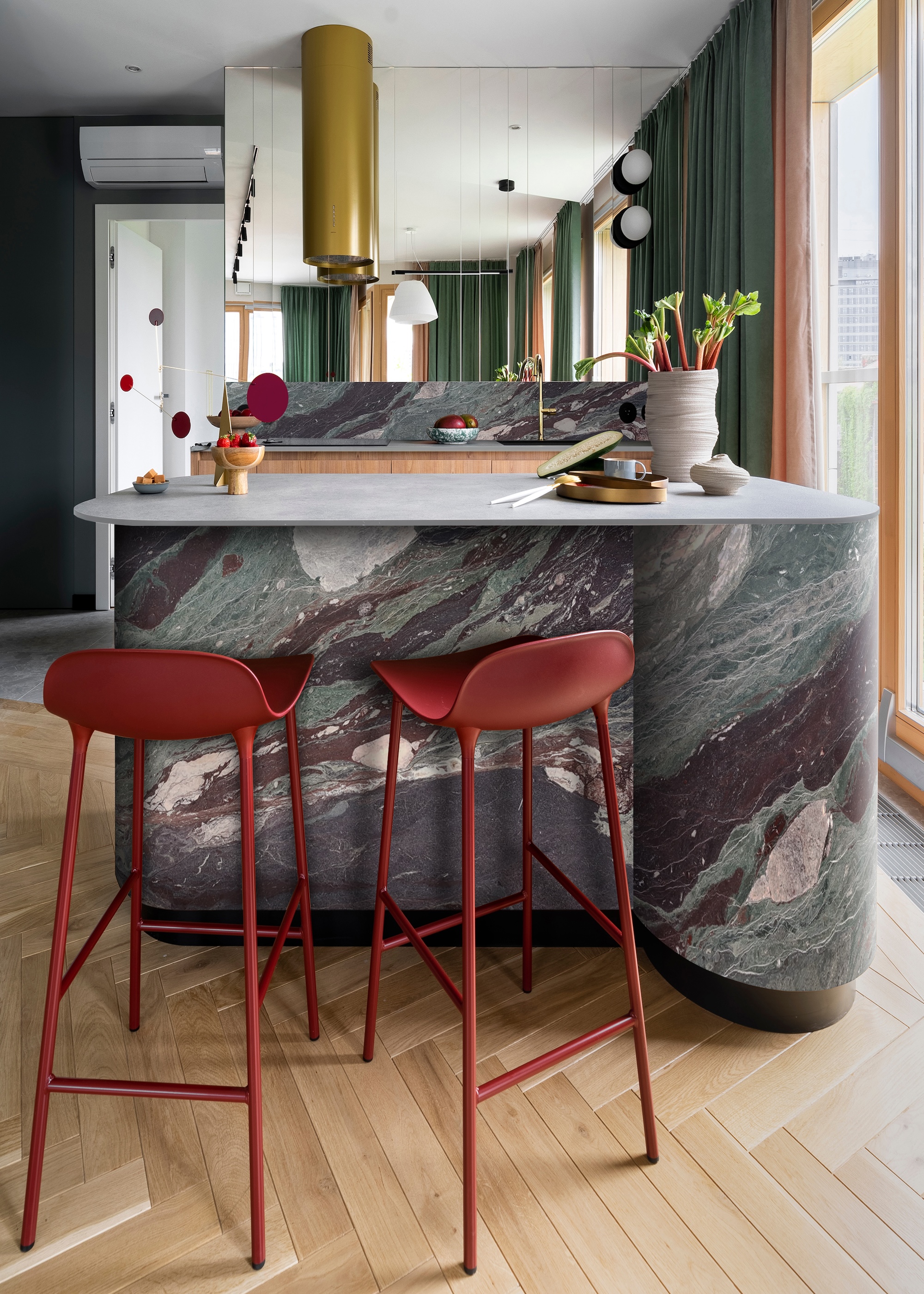 A curved small kitchen island with red stools beside it and above are two golden lights.
