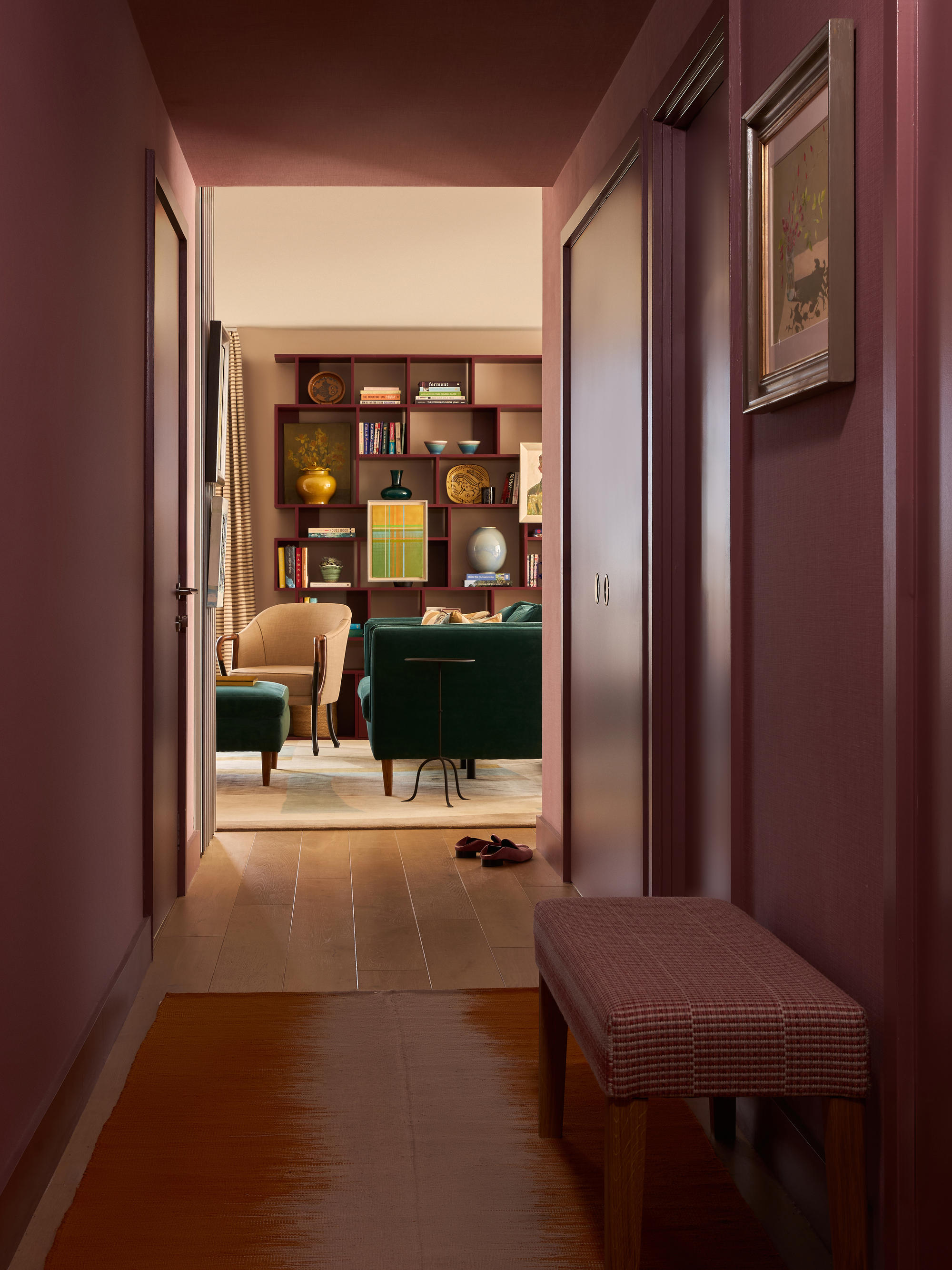 hallway with timber floorboards, orange rug, bench seat, pink walls and ceiling, artwork, and view through to the living room