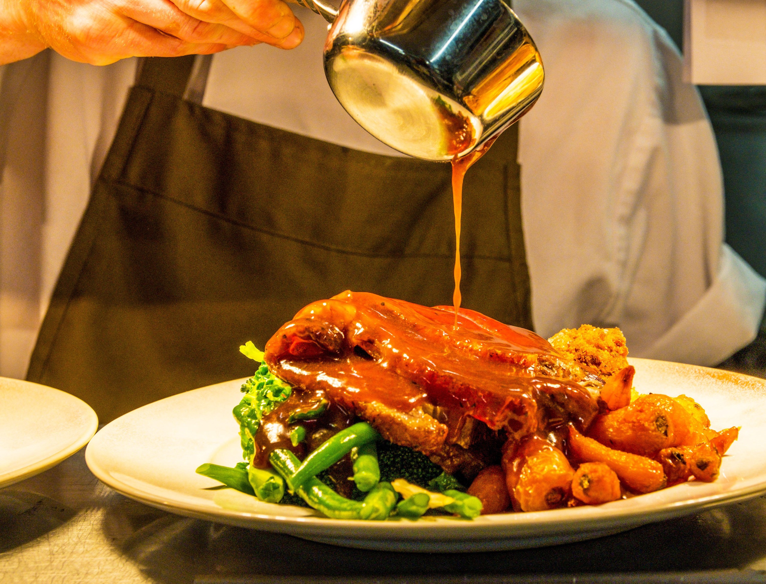 A chef pours gravy onto a sunday roast