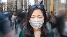 A woman wearing a mask stands on the street in New York City.