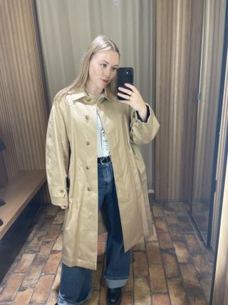 Woman in mirror wears camel trench coat, blue jeans, white T-shirt