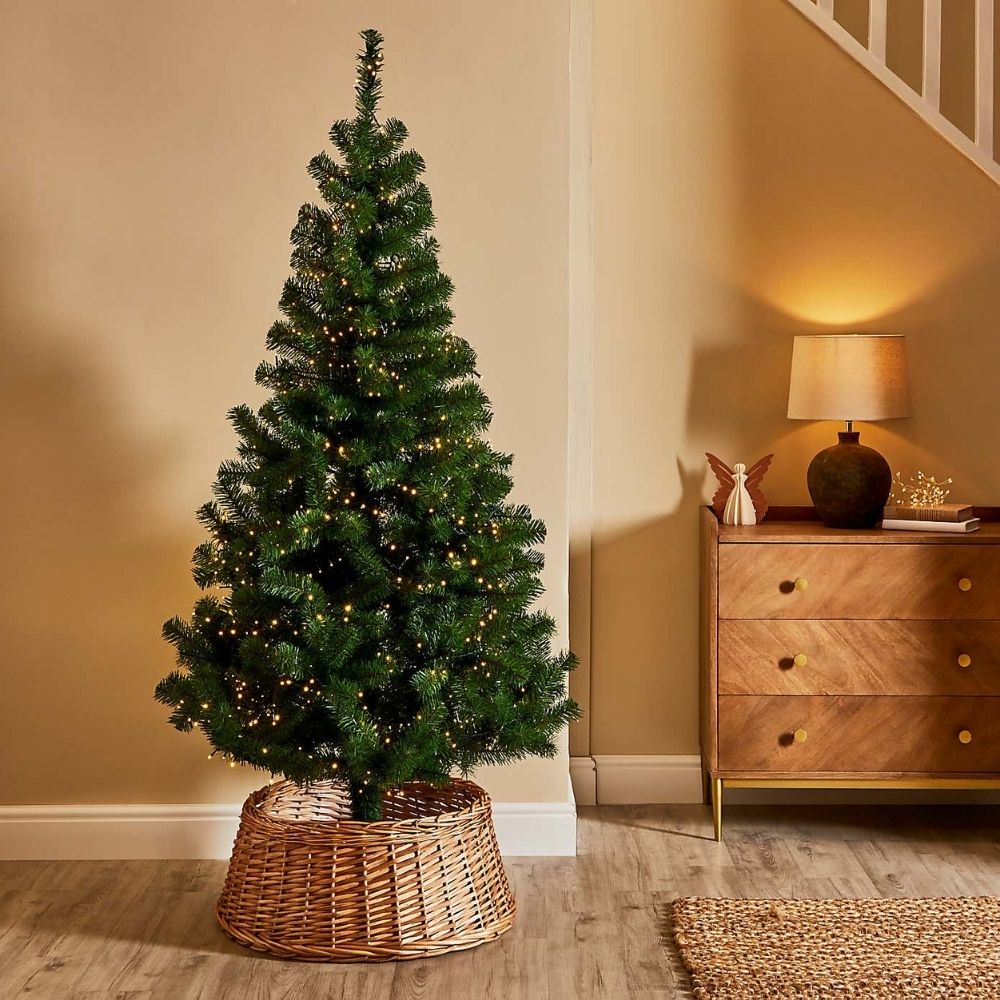 Dunelm 6ft green Christmas tree in a yellow living room next to a chest of drawers.