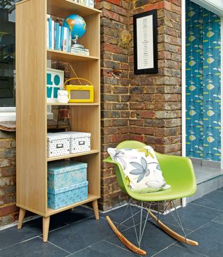 Conservatory with exposed brick wall and tall wooden storage unit, with a modern green rocking chair in front of it