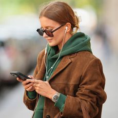  Diane Batoukina wears light brown hair styled in a low bun, oversized square sunglasses by Kaleos, a brown suede leather blazer jacket, a green WRSTBHVR hoodie with white printed logo, during a street style fashion photo session, on September 05, 2025 in Paris, France. (Photo by Edward Berthelot/Getty Images)