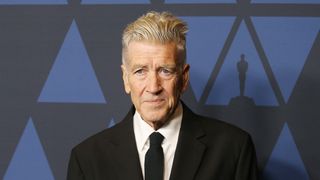 a white-haired man in a black suit on a red carpet