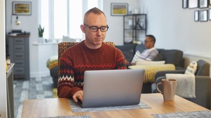 A man works on his laptop, getting his digital estate planning in order, at the dining room table.