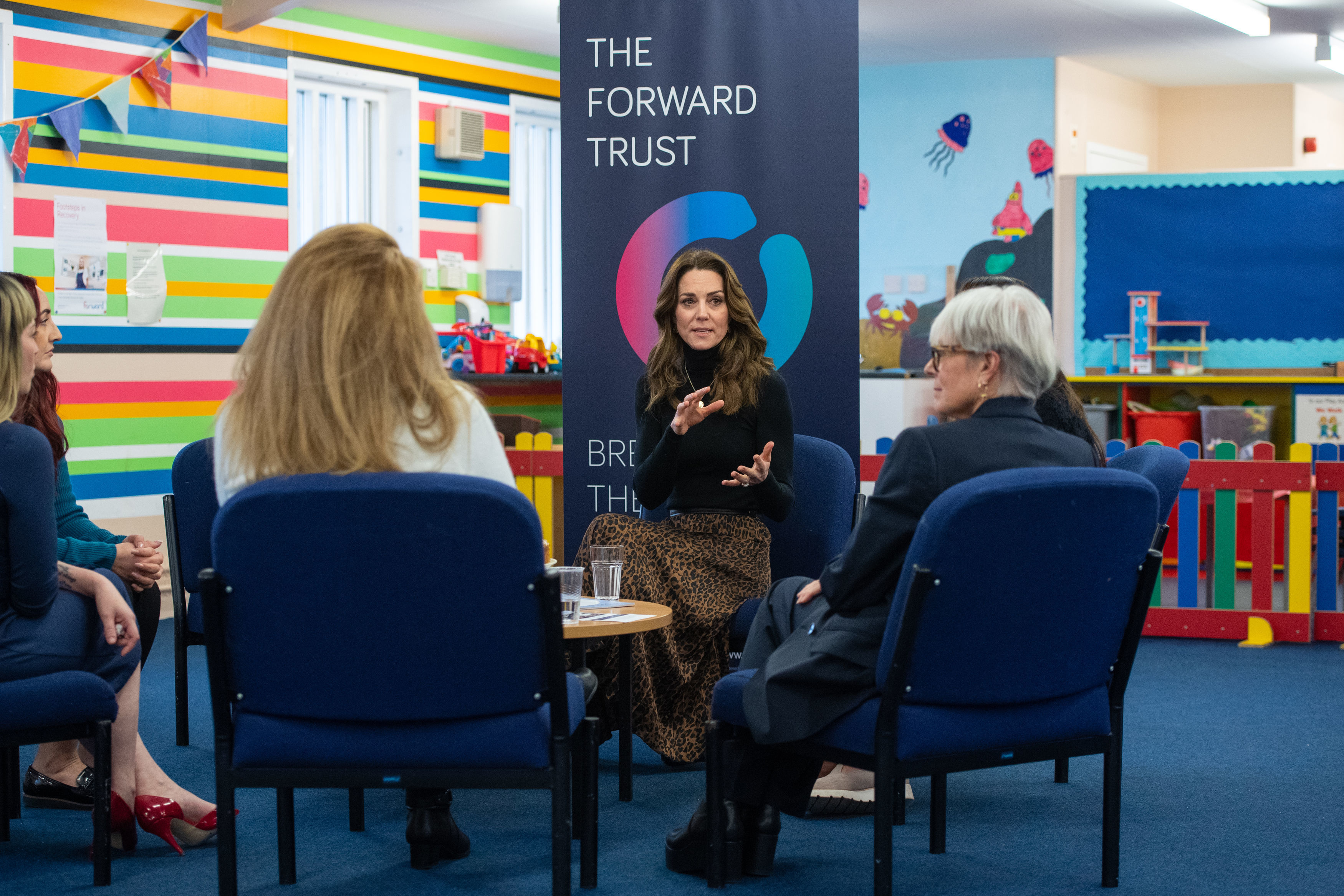 Kate Middleton sitting in a chair talking to people in front of a banner that says The Forward Trust