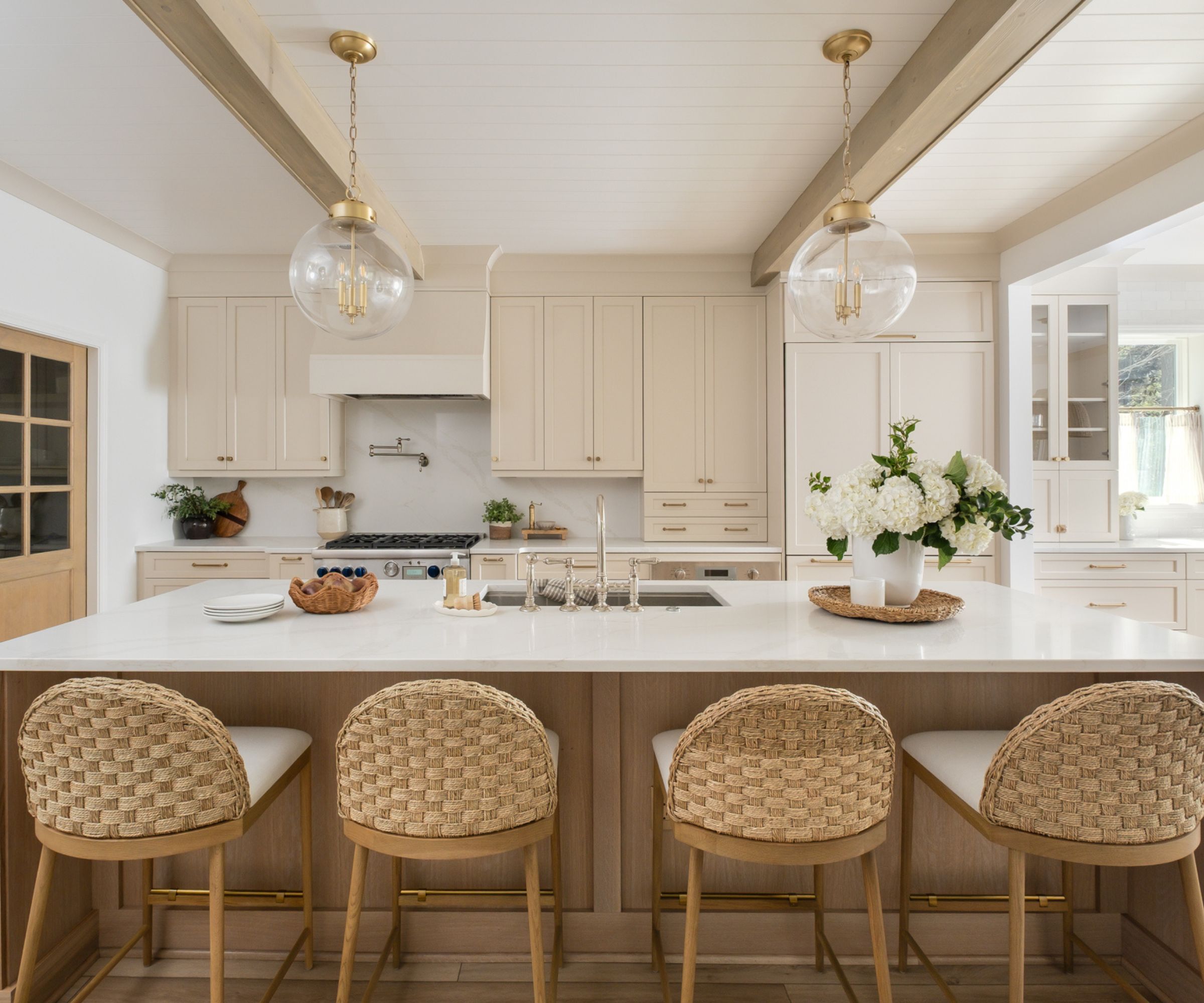 A coastal kitchen with warm white cabinets, white countertops, and wooden decor