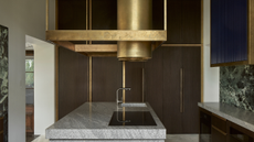 a modern luxury kitchen with granite work surfaces, wooden cabinets, a marble backsplash, and a gold extractor fan