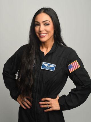 a woman in a dark jumpsuit with an american flag patch on her left shoulder, and a flight wings patch on the left side of her chest.