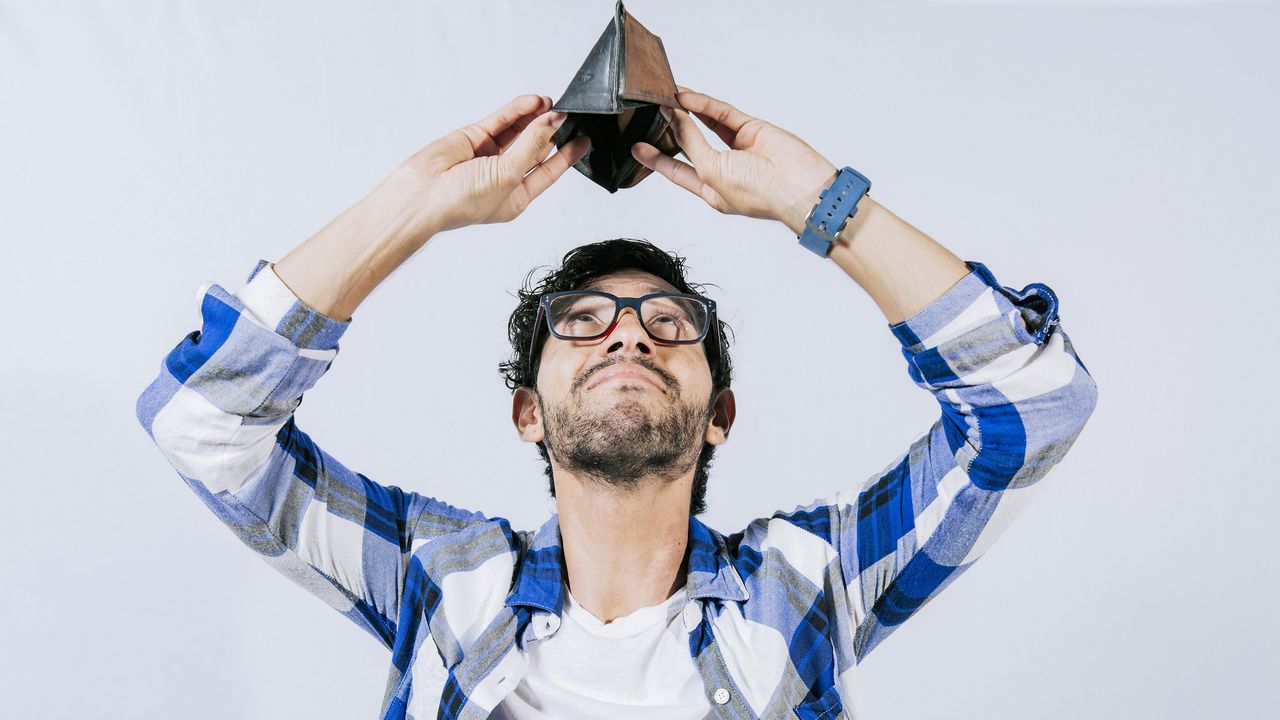 A young man holds his empty wallet above his head as he looks into it.