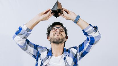 A young man holds his empty wallet above his head as he looks into it.