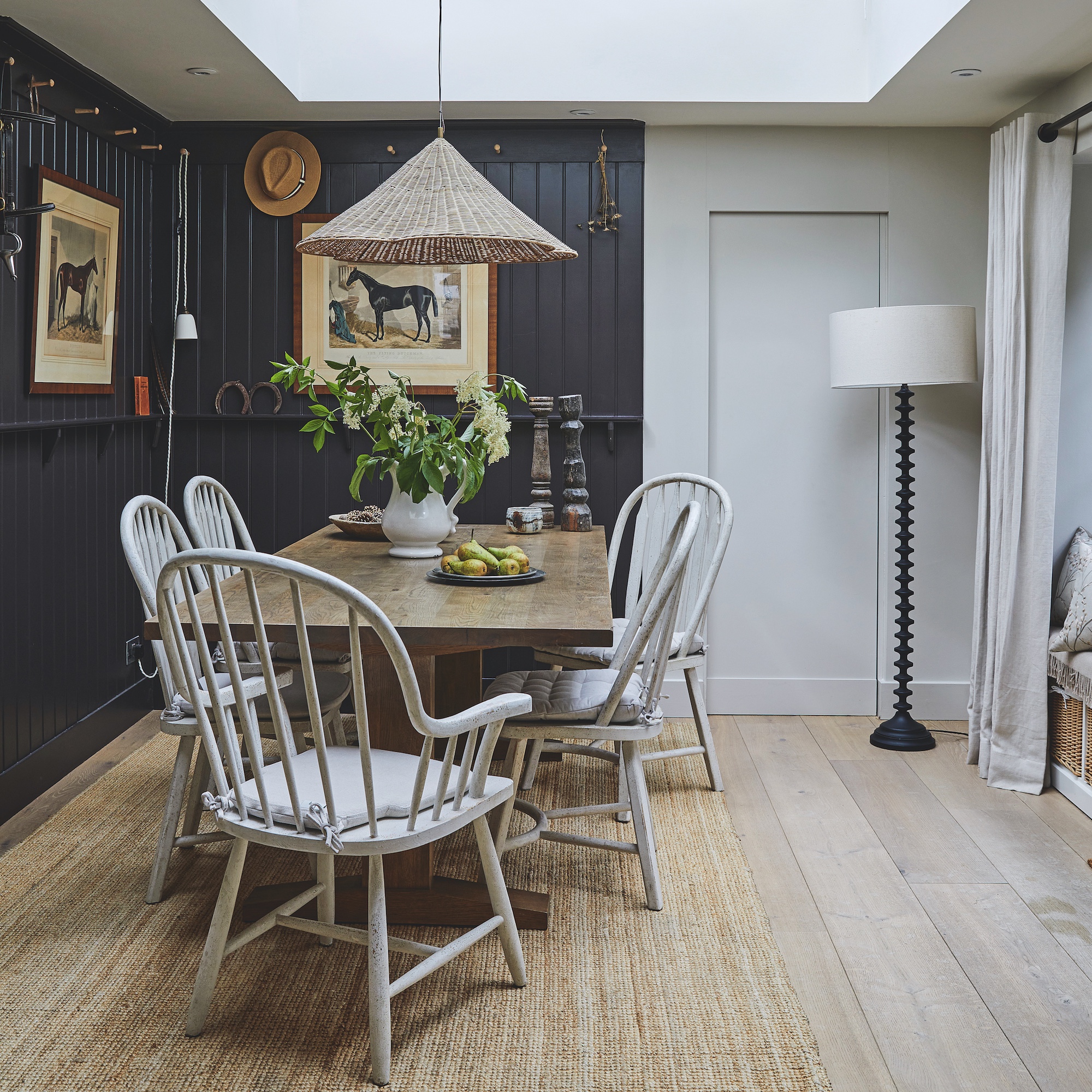dining area with tongue and groove dark charcoal wooden panelling, a wooden farmhouse style table, and white farmhouse style chairs, with a rush rug and rattan pendant light