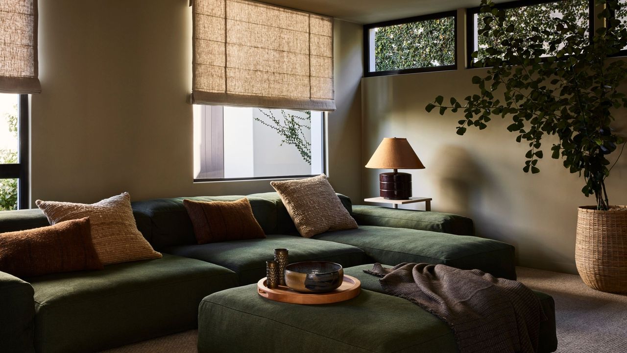 a cozy living room with olive green sofa and cream walls and curtains