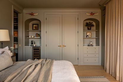 A neutral bedroom with built in decorative wall storage and wall lights