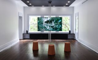 Room with large window, wooden floors, tan stools in front of LED display