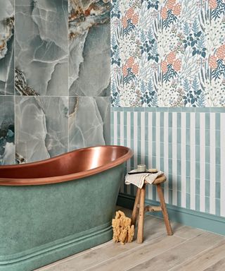 A blue green bathroom with marble wand wallpaper walls and a green and copper bath