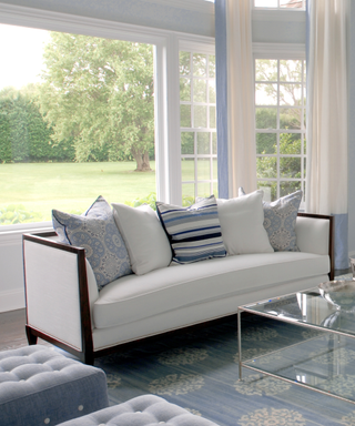 A white sofa with blue cushions and a large picture window.