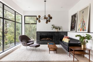 Living room with black-framed corner windows, black leather sofa, beige rug and black tiled fireplace