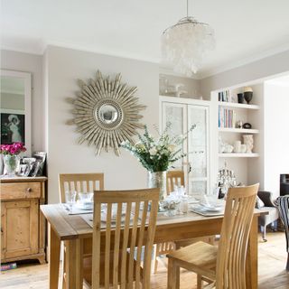 White dining room with wooden table and chairs, sunburst mirror and pendant light