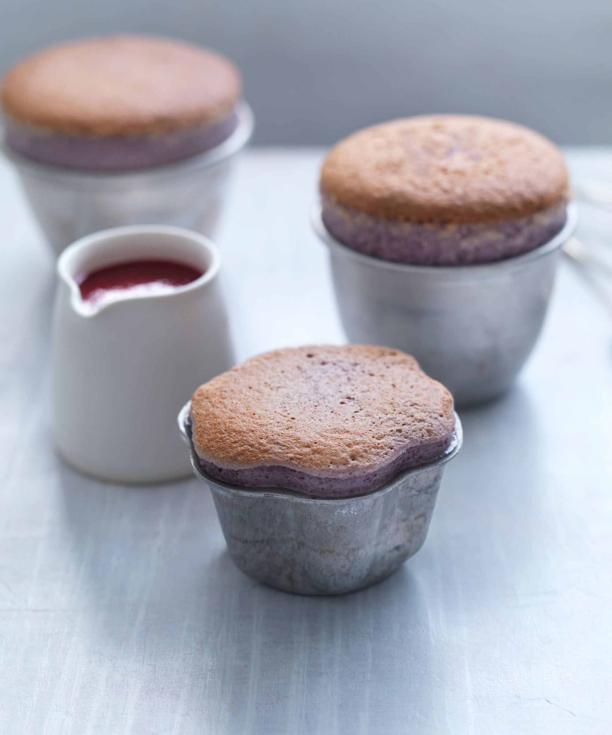 Three souffles in dishes with a jug of cherry sauce