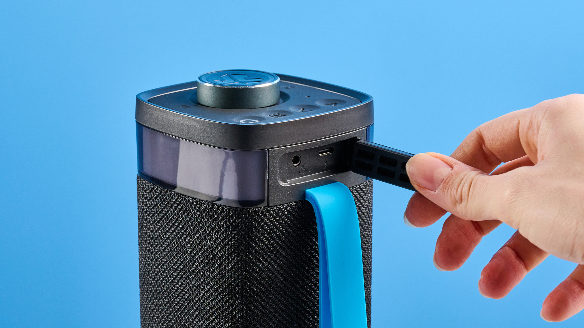the jlab jbuds party speaker with LED rainbow lights photographed against a blue background