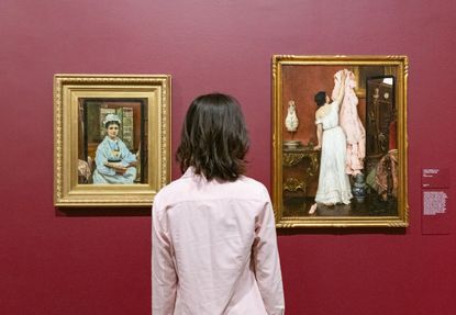 back of womans head looking at paintings on red wall