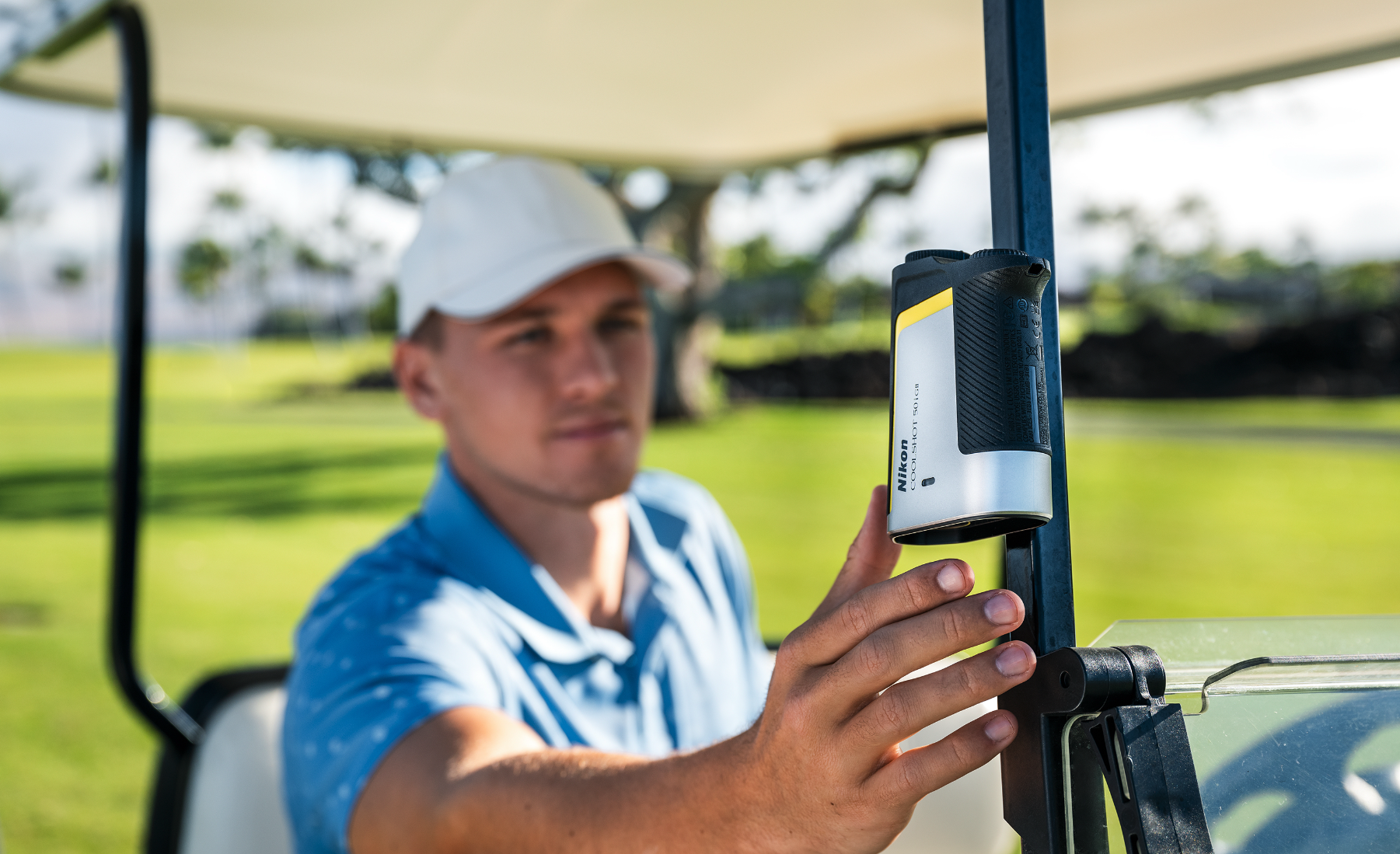 A golfer reaching for their rangefinder which is magnetically attached to their cart