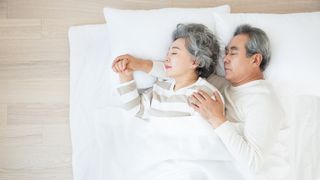 Why is sleep important: A senior couple cuddle while sleeping in a white bed