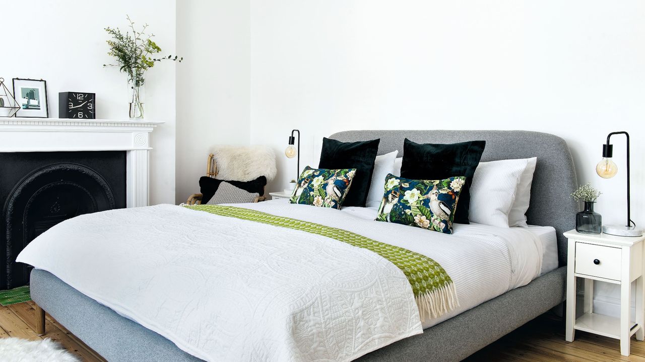 Bedroom with white walls, wooden floorboards, double bed with grey headboard and black and white bedding