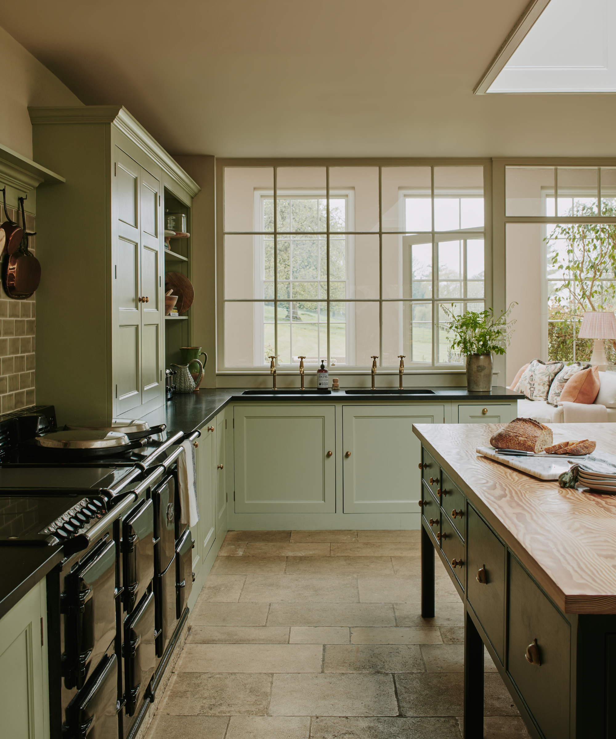 a large kitchen with sage green cabinetry, a freestanding island with a wooden slab surface, a large oven, and windows that look out to a yard