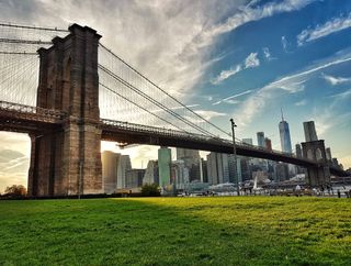 A view of the Brooklyn Bridge at sunset from Empire Fulton Ferry Lawn at Brooklyn Bridge Park with lower Manhattan in the background including One World Trade Center