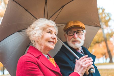 A senior couple sharing an umbrella while walking through the park.