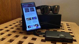 TCL Nxtwear S AR glasses with their adapter and a smartphone showing the TechRadar home page