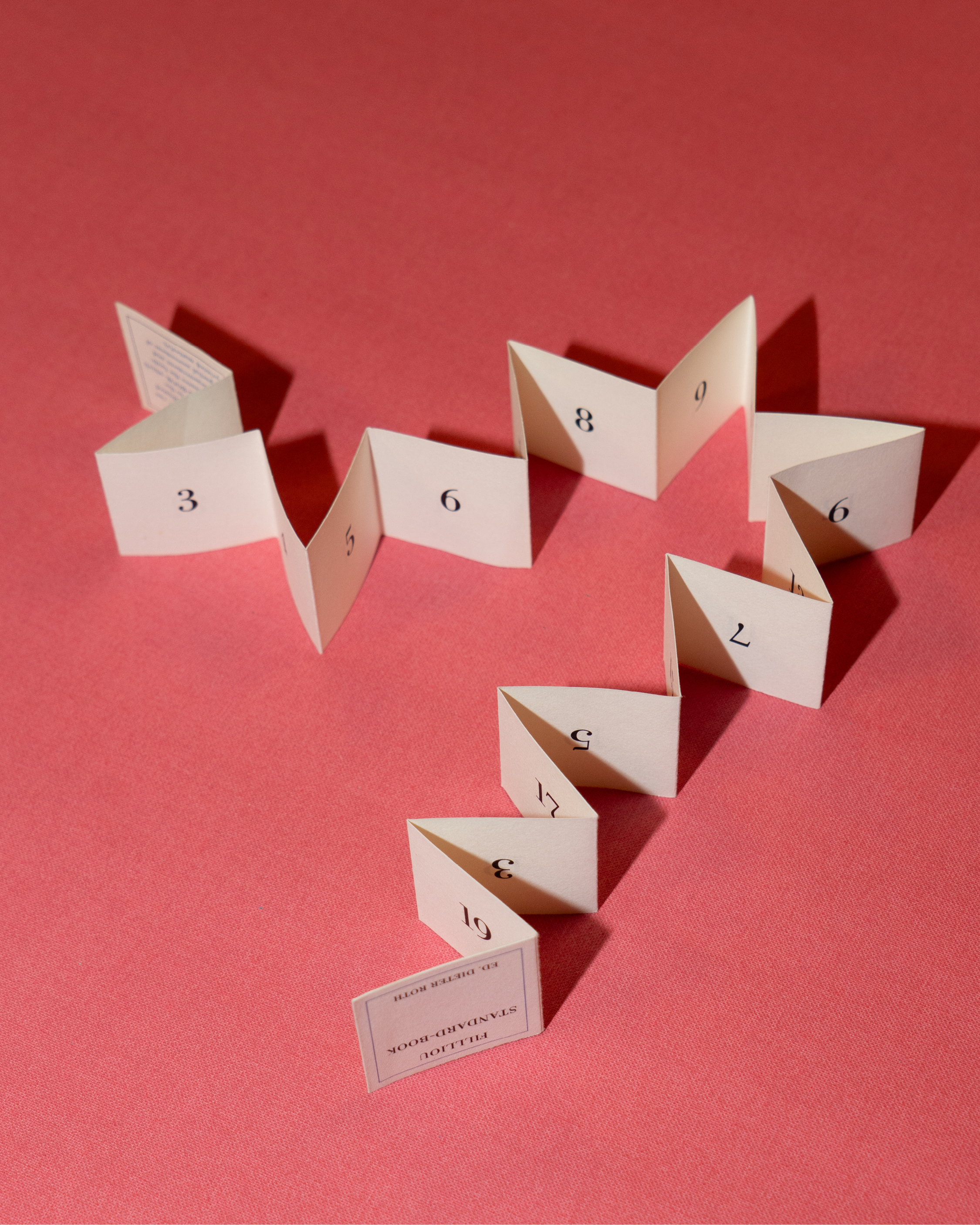 small folded book arranged across a pink backdrop