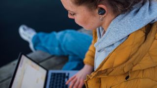 Beyerdynamic Free Byrd lifestyle image showing female outdoors with laptop and wearing earbuds