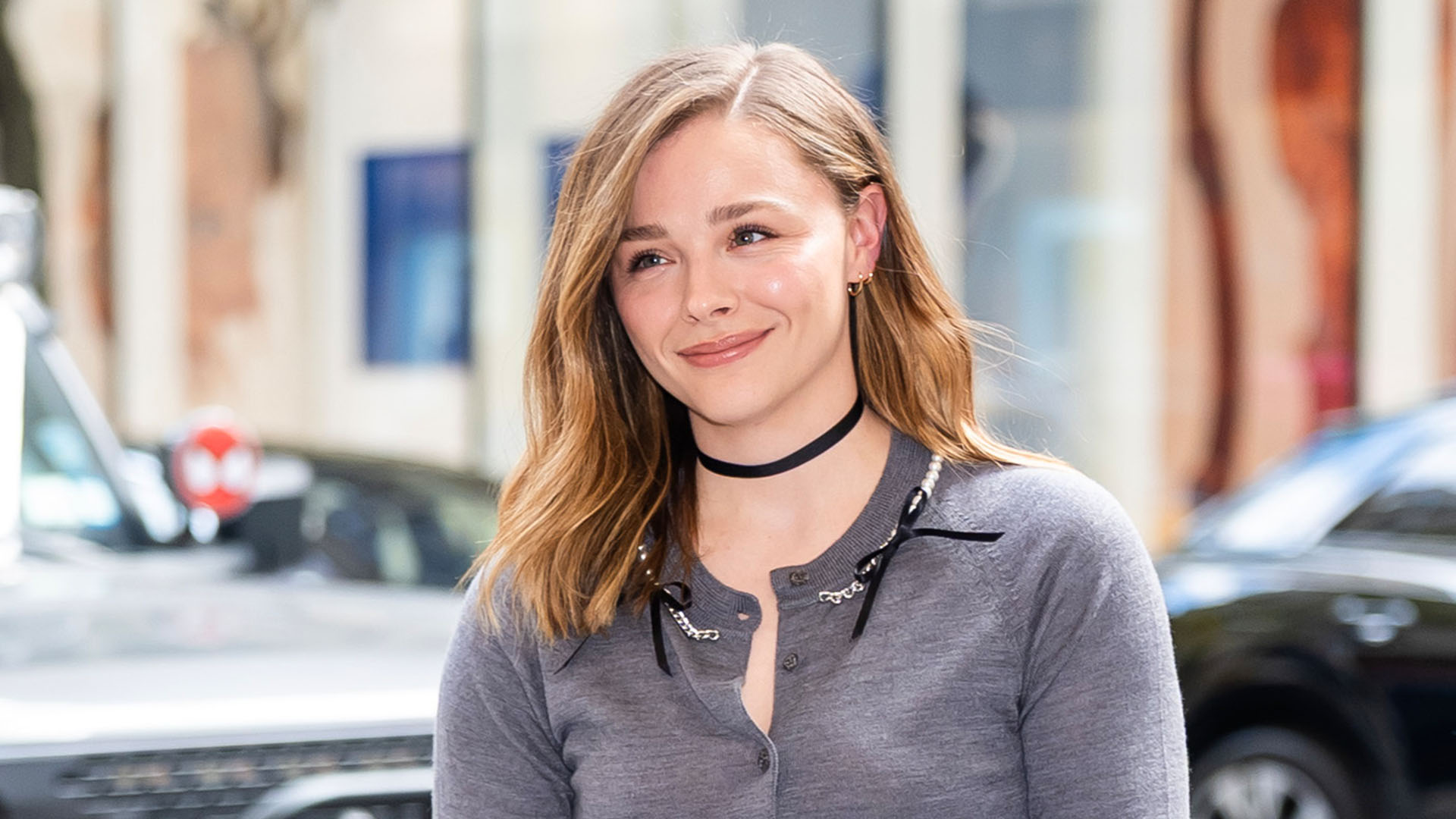 Chloe Grace Mortez wearing a gray cardigan, black fringe skirt, and black thigh high boots