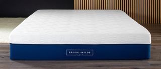 Brook + Wilde Suprema Mattress review image shows the mattress placed on a hard wood floor in front of a wooden backdrop
