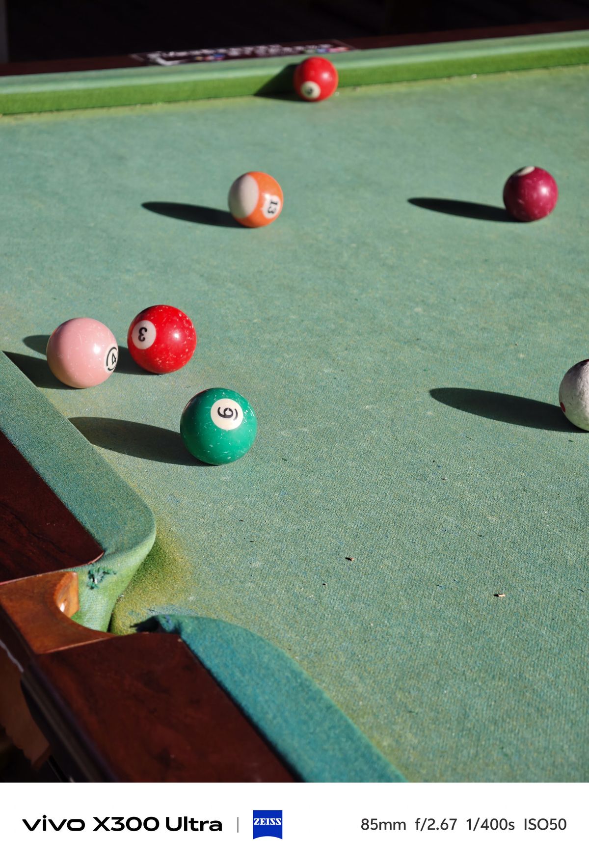 Several billiard balls scattered across a worn green pool table felt casting long shadows.