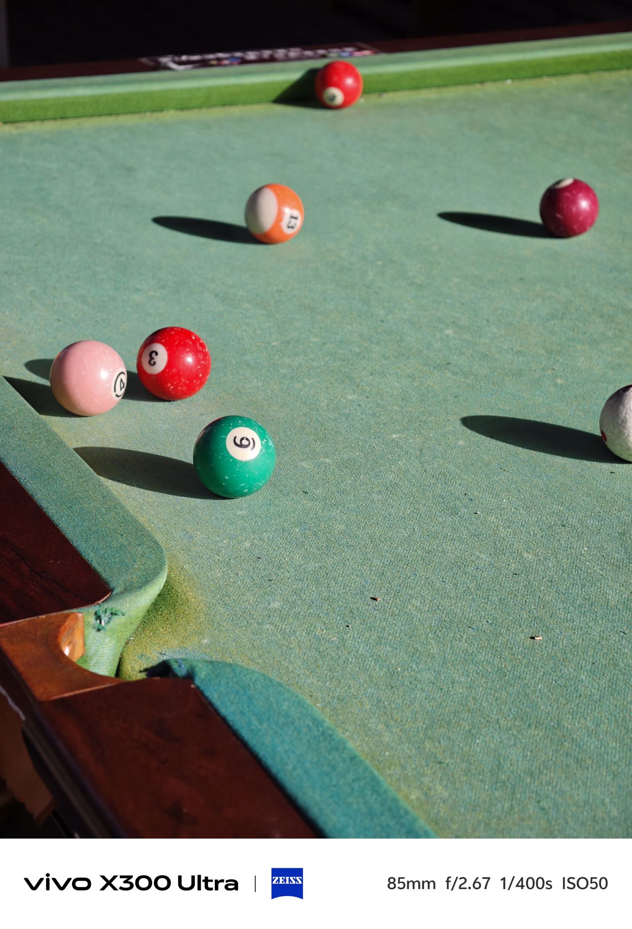 Several billiard balls scattered across a worn green pool table felt casting long shadows.