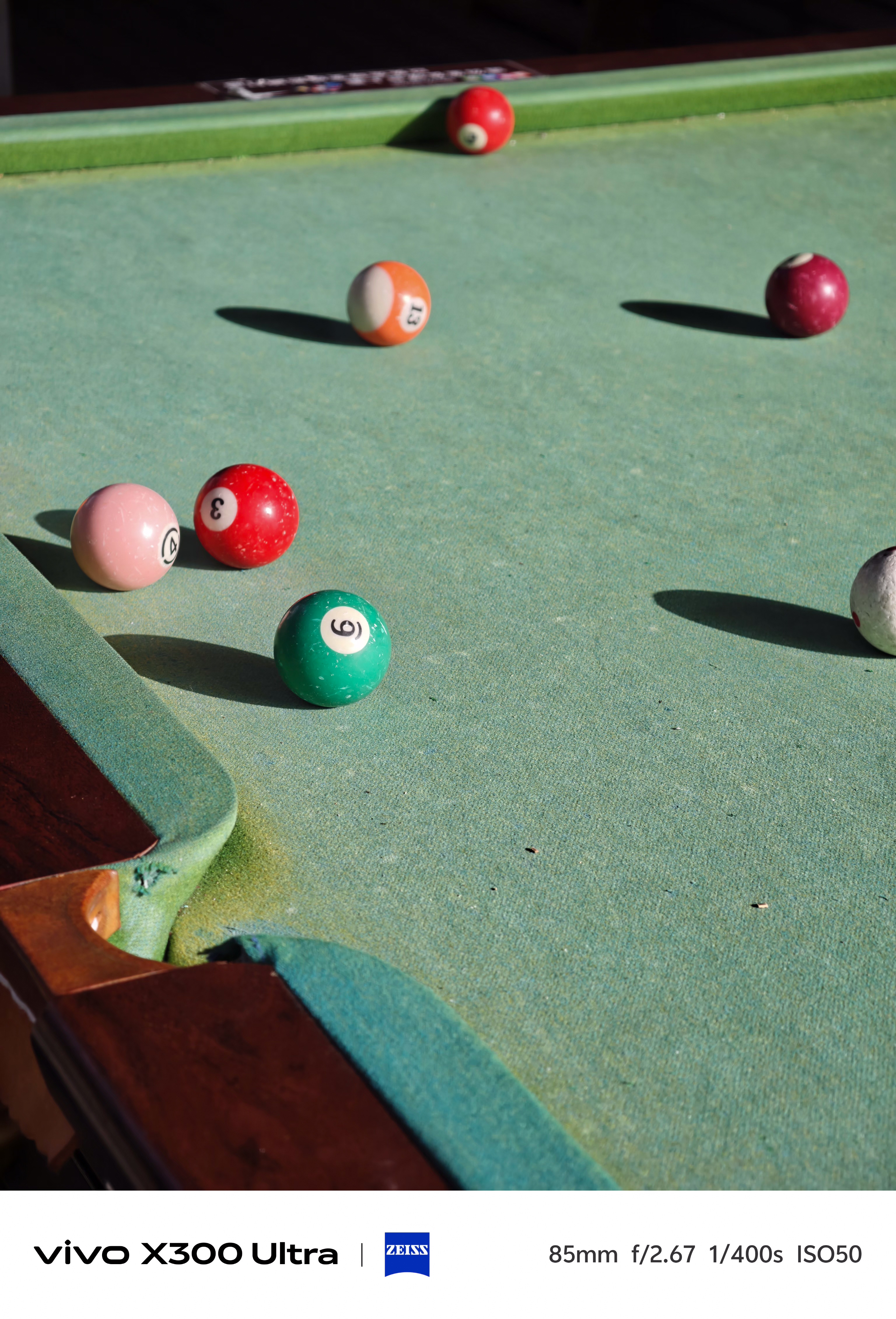 Several billiard balls scattered across a worn green pool table felt casting long shadows.