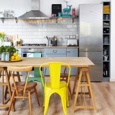 Blue kitchen with wooden worktops and floor, a stainless steel fridge freezer and a yellow bistro chair